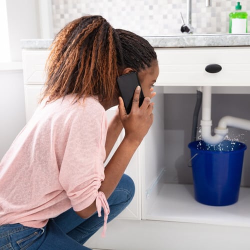 woman calling a plumber while taking care of a leaking pipe