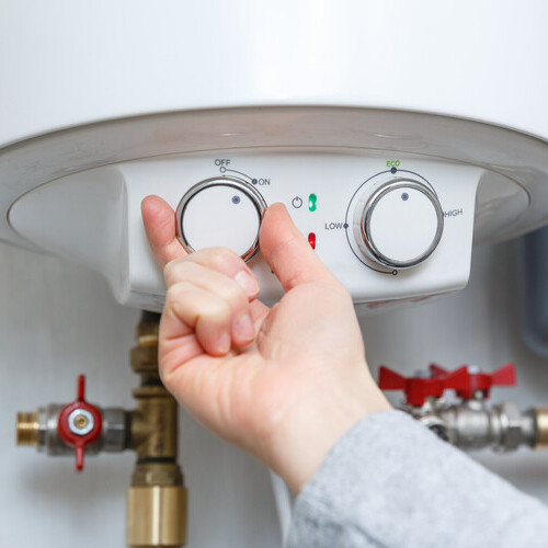close-up of a hand turning a knob on a hot water heater