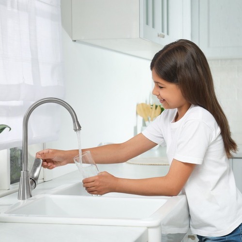 a young girl at a sink pouring a glass of water