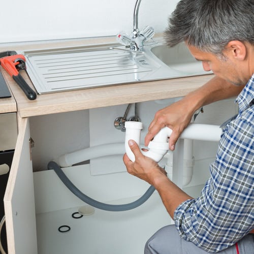 plumber fixing pipes underneath a sink